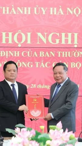 Phó Bí thư Thường trực Thành ủy Hà Nội Nguyễn Văn Phong trao quyết định của Ban Thường vụ Thành ủy Hà Nội và tặng hoa chúc mừng ông Vũ Minh Tuấn. (Ảnh: Quang Thái)