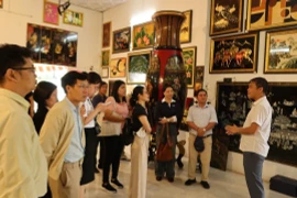 Khách tham quan lắng nghe giới thiệu về lịch sử tranh sơn mài tại cơ sở sản xuất sơn mài Định Hoà. (Ảnh: Khánh Ly/Vietnam+)