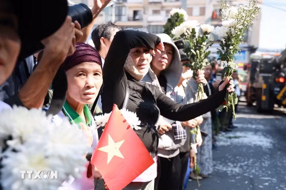 Người dân cầm hoa chờ tiễn đoàn xe đưa liệt sỹ. (Ảnh: Mạnh Minh/TTXVN)