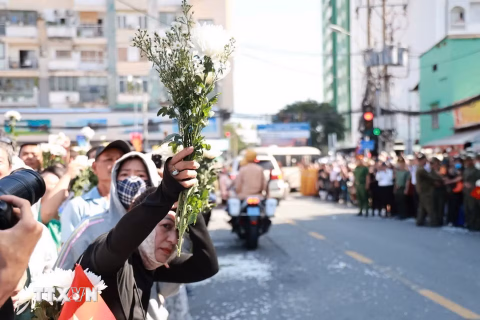 Người dân cầm hoa chờ tiễn đoàn xe đưa liệt sỹ. (Ảnh: Mạnh Minh/TTXVN)