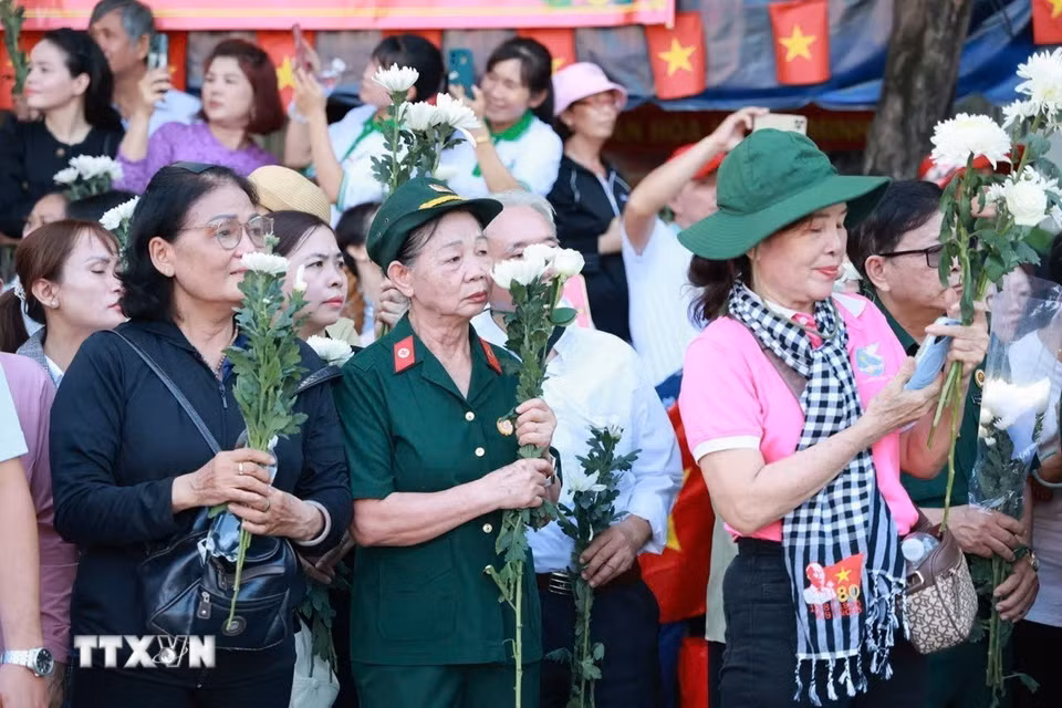 Người dân cầm hoa chờ tiễn đoàn xe đưa liệt sỹ. (Ảnh: Mạnh Minh/TTXVN)