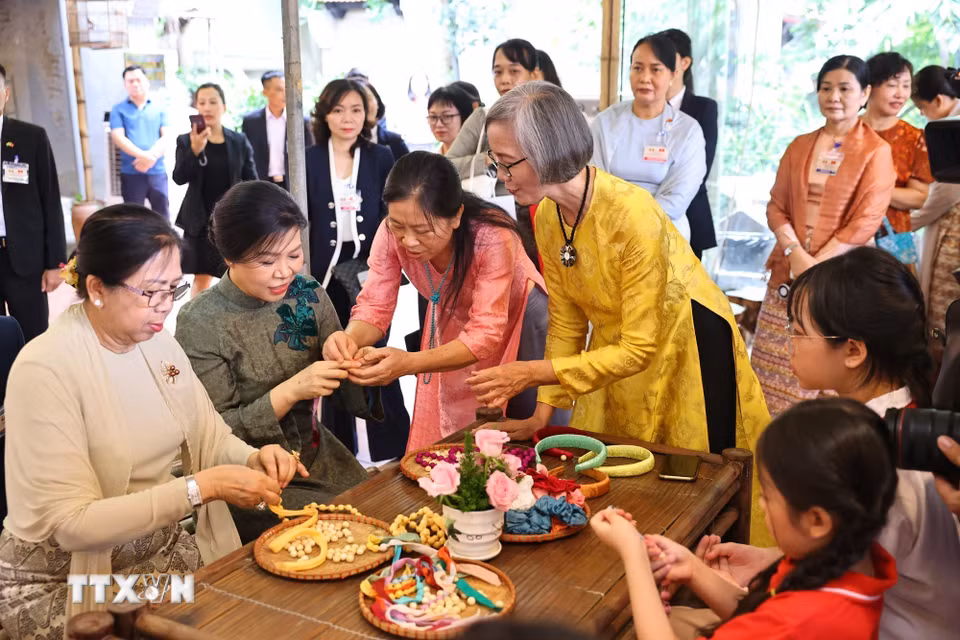 Phu nhân Ngô Phương Ly và Phu nhân Kyu Kyu Hla trải nghiệm xâu vòng lụa với các cháu thiếu niên, nhi đồng của làng nghề. (Ảnh: Minh Đức/TTXVN)