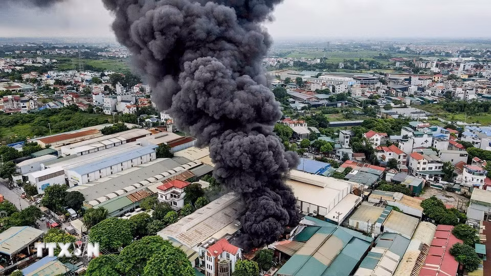 Cột khói đen dày đặc bốc lên từ khu vực xưởng nhựa; lực lượng chức năng triển khai nhiều mũi tiếp cận hiện trường để khống chế đám cháy. (Ảnh: TTXVN phát)