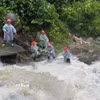 Lực lượng chức năng căng dây để trục vớt thi thể người đàn ông dưới dòng nước chảy siết. (Ảnh: TTXVN phát)