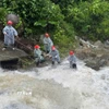 Lực lượng chức năng căng dây để trục vớt thi thể người đàn ông dưới dòng nước chảy siết. (Ảnh: TTXVN phát)