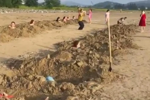 Nhóm du khách nằm dưới các hố cát tự đào trên bãi biển Cửa Lò. (Ảnh cắt từ clip).