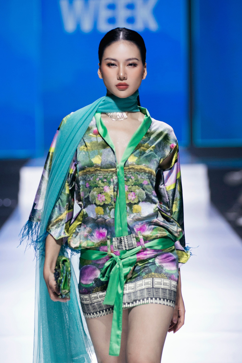 Miss Universe Vietnam 2023 Bùi Quỳnh Hoa xuất hiện mở màn cùng những bước catwalk quyến rũ. Trong chiếc váy lụa họa tiết hoa sen tinh tế kết hợp cùng khăn voan quàng cổ và chiếc ví xanh “tone - sur - tone,” Hoa hậu Bùi Quỳnh Hoa trở thành tâm điểm trên sàn diễn. (Ảnh: CTV/Vietnam+)