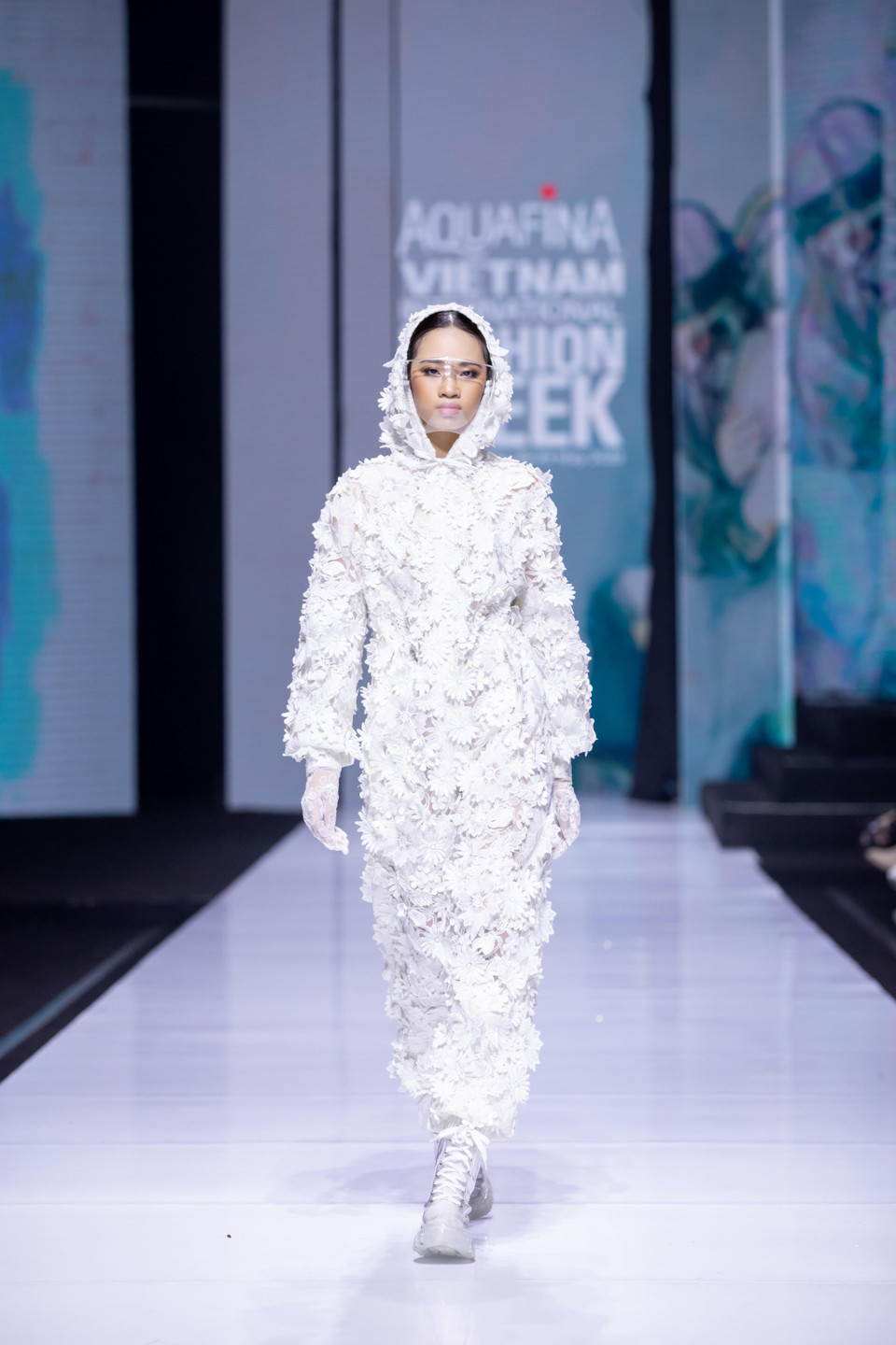 Thiết kế chủ đạo được thể hiện qua màn catwalk ấn tượng của mẫu nhí Almira Bảo Hà trong bộ jumpsuit trắng - thiết kế tương đồng nhất với bộ quần áo bảo hộ kết hợp cùng kính chống giọt bắn quen thuộc trong khoảng thời gian đại dịch. (Ảnh: CTV/Vietnam+)