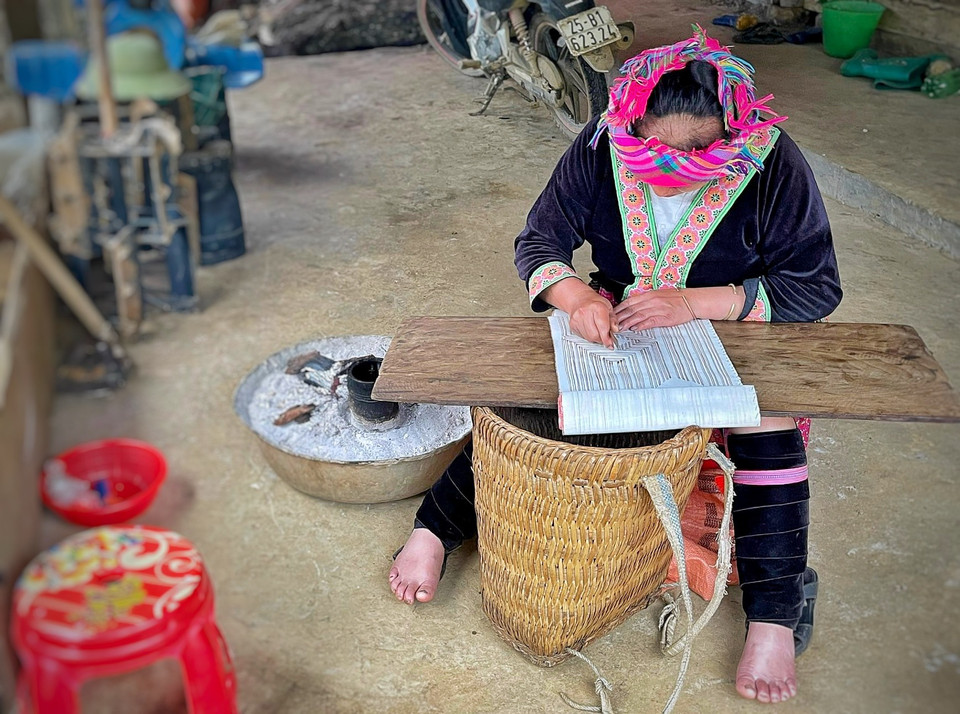 Công đoạn làm nên hồn cốt của vải lanh thổ cẩm người H’Mông là vẽ sáp ong lên tấm vải lanh được dệt từ sợi lanh có màu trắng ngà. Để có hoa văn, người phụ nữ H’Mông dùng sáp ong. Theo bà Chai, sáp ong có hai khoảnh màu vàng và màu nâu. Màu vàng là sáp non, màu nâu là lớp sáp già, bóp cho hai loại sáp đó chảy hết mật rồi nấu mỗi loại ra một nồi khác nhau. Nấu mật sáp ong cho đến khi nóng chảy thành nước cốt, lấy mỗi thứ một ít bỏ vào bát, trộn đều và đặt lên bếp. Nếu trộn hai thứ ngay từ đầu thì lên váy không được đẹp. Chảo để nấu sáp ong bao giờ cũng để nóng ở trên bếp. Nếu không nóng như thế, sáp sẽ bị khô và không dính vào váy. (Ảnh: Xuân Mai/Vietnam+)