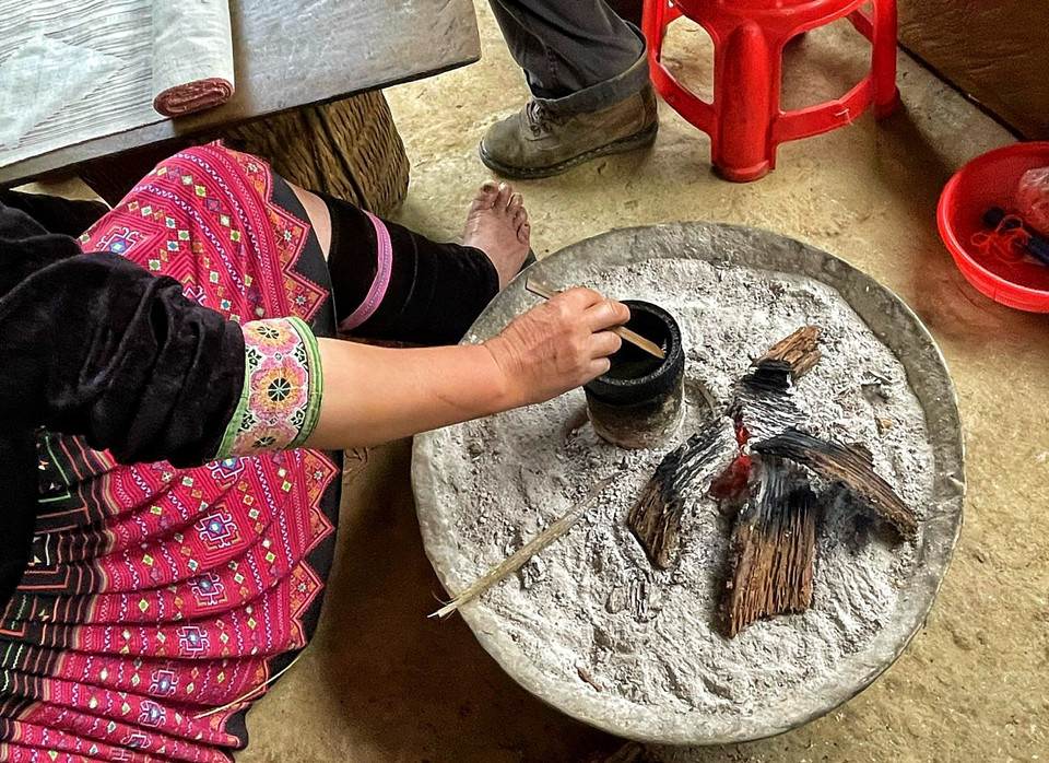 Vì sao người H’Mông dùng sáp ong để vẽ? Bởi khi công đoạn này hoàn thành, cả tấm vải sẽ đem nhuộm chàm, chỗ không có sáp ong nhuộm thành chàm đen, còn chỗ có sáp ong, chàm không thấm vào được sẽ tạo thành các hoạ tiết độc đáo. Sau đó, người ta nấu chảy sáp ong đi, những hoa văn được vẽ bằng sáp ong sẽ trở thành màu trắng xanh, làm nổi bật trang phục.(Ảnh: Xuân Mai/Vietnam+)