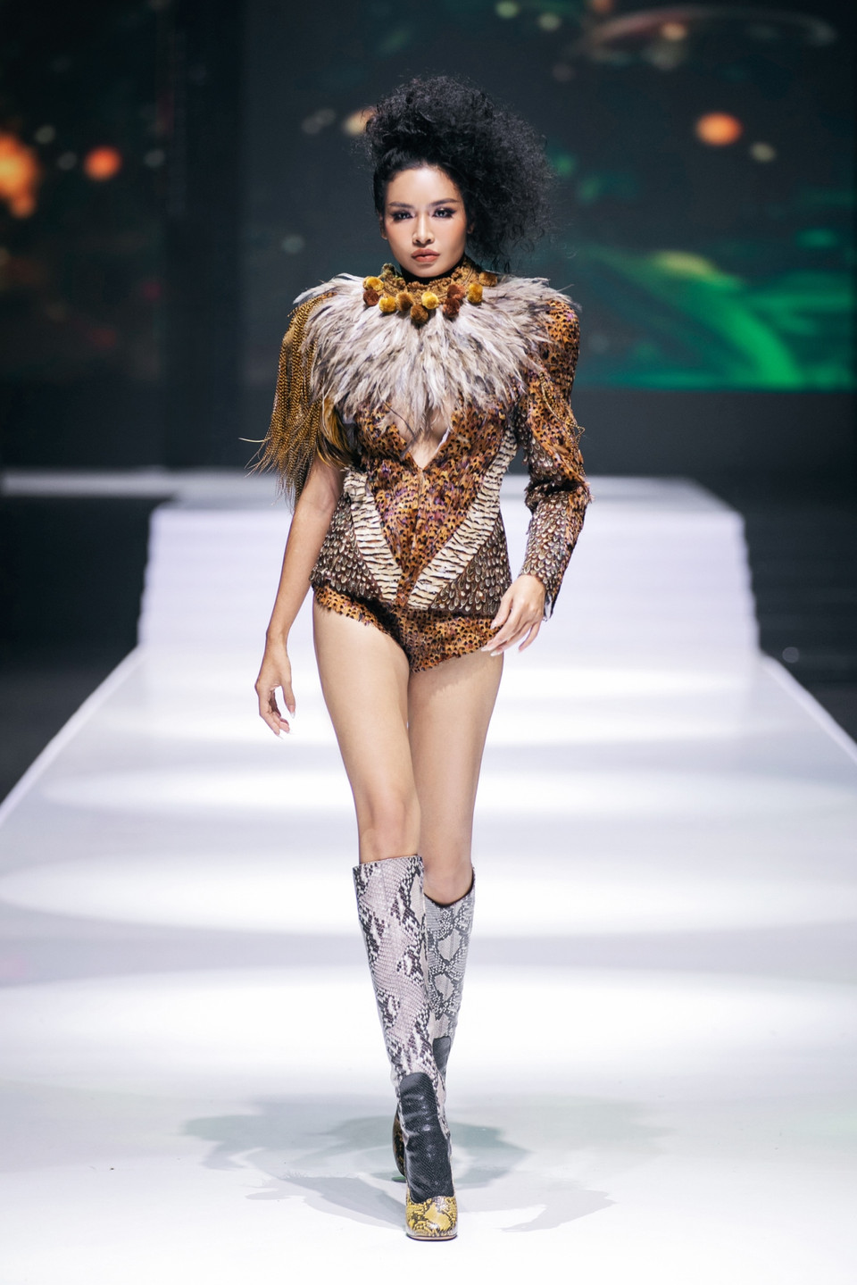 Mở màn cho "Down To Earth," Miss Cosmo Thailand - Mook Karnruethai Tassabut xuất hiện trong thiết kế độc đáo. Diện bộ cánh được xẻ ngực táo bạo ẩn hiện dưới lớp lông vũ mềm mại, kết hợp cùng dáng quần soóc ngắn và đôi bốt da hầm hố, nàng hậu đã tạo nên tổng thể vừa hoang dã, phóng khoáng, vừa quyến rũ, bí ẩn. (Ảnh: PV/Vietnam+)