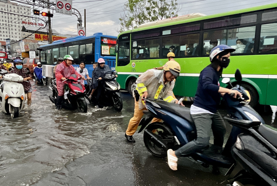 CSGT lội nước, dầm mưa, vừa điều tiết giao thông, vừa giúp người dân vượt qua vùng trũng, ngập úng sâu ở đoạn Quốc lộ 50 - Nguyễn Văn Linh, Quận 8. (Ảnh: Thanh Vũ/TTXVN)