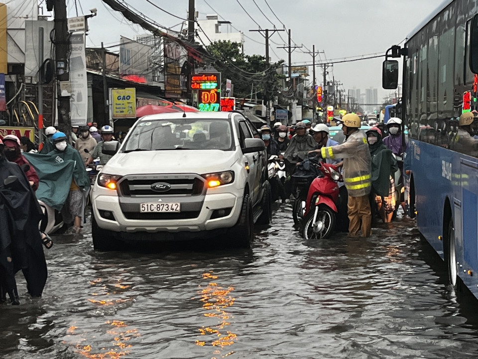 CSGT lội nước, dầm mưa, vừa điều tiết giao thông vừa giúp người dân vượt qua vùng trũng, ngập úng sâu ở đoạn Quốc lộ 50 - Nguyễn Văn Linh, Quận 8. (Ảnh: Thanh Vũ/TTXVN)