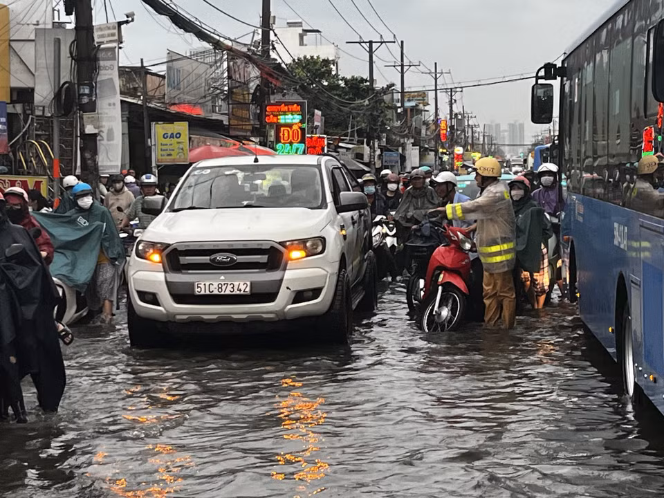 CSGT lội nước, dầm mưa, vừa điều tiết giao thông vừa giúp người dân vượt qua vùng trũng, ngập úng sâu ở đoạn Quốc lộ 50 - Nguyễn Văn Linh, Quận 8. (Ảnh: Thanh Vũ/TTXVN)