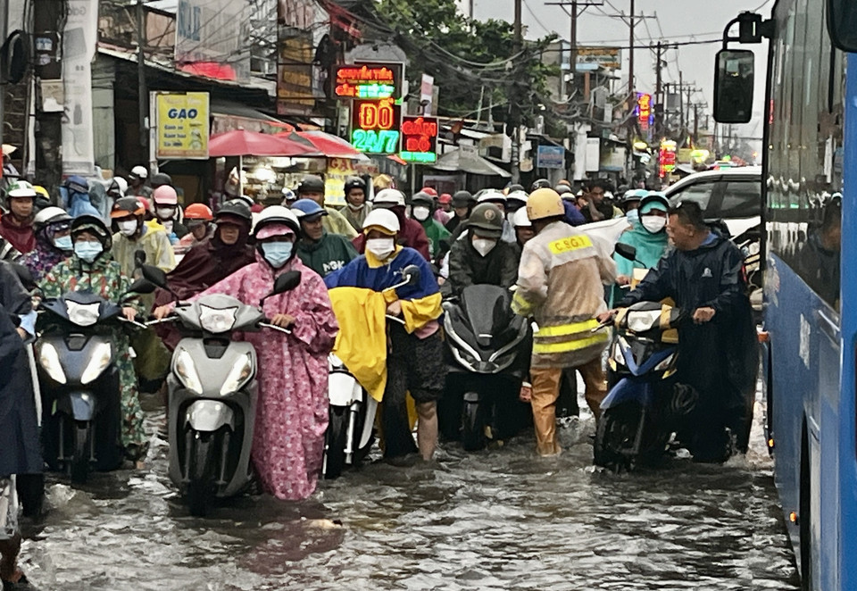 CSGT lội nước, dầm mưa, vừa điều tiết giao thông, vừa giúp người dân vượt qua vùng trũng, ngập úng sâu ở đoạn Quốc lộ 50 - Nguyễn Văn Linh, Quận 8.( Ảnh: Thanh Vũ/TTXVN)