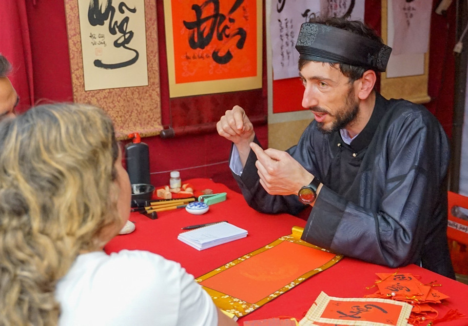 Ông đồ Tây đang giải thích ý nghĩa của chữ sắp viết cho du khách nước ngoài. (Ảnh: Khánh Hòa/TTXVN)