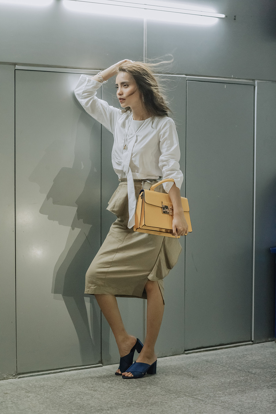 Linh Chi hóa thân thành cô nàng công sở điệu đà khi kết hợp chiếc áo sơ mi trắng đơn giản cùng chân váy màu be có điểm nhấn là họa tiết bèo nhún dọc chân váy, kèm túi màu nâu sáng