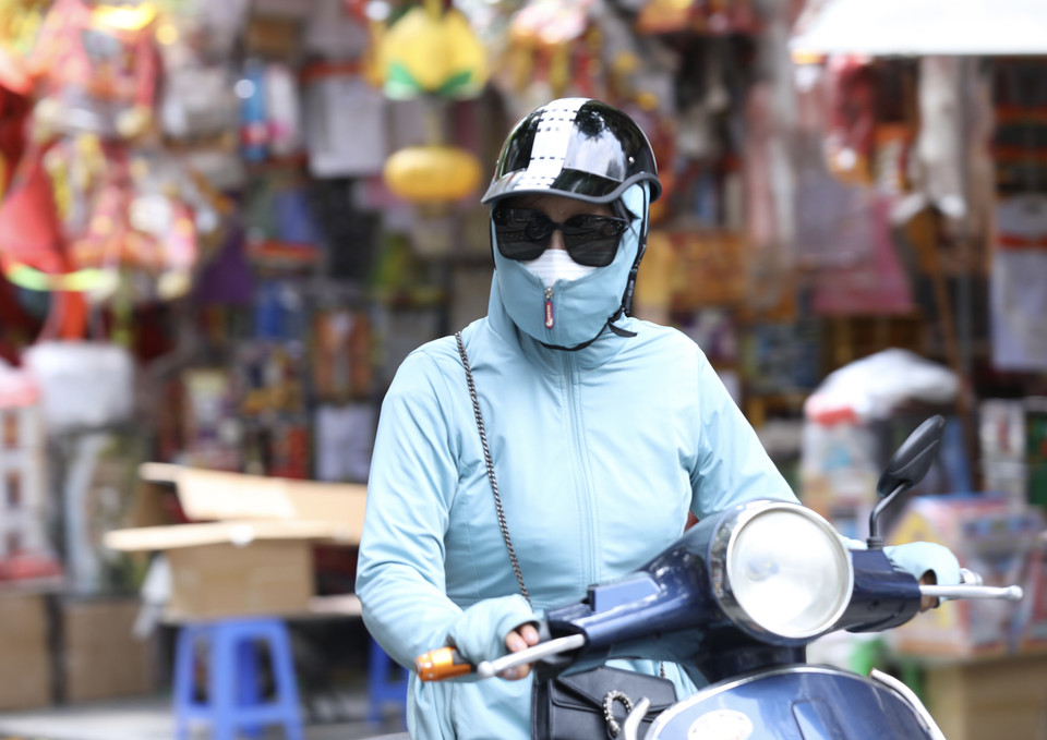 Người dân mặc đồ kín mít tránh nắng, nóng khi phải di chuyển trên đường ngày 28/6. (Ảnh: Hoàng Hiếu/TTXVN)