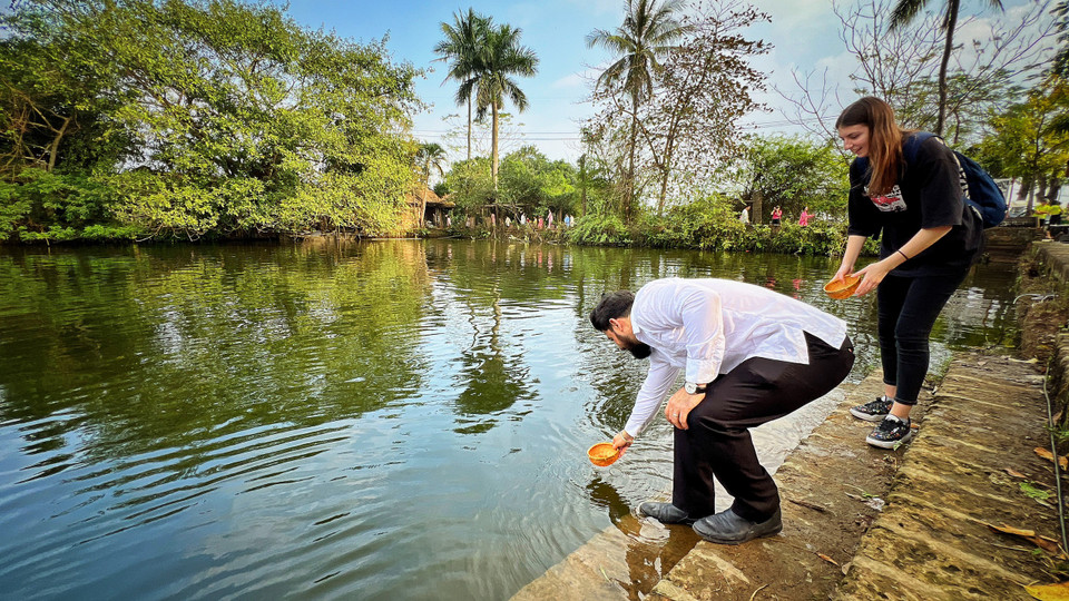 Du khách quốc tế thích thú khi được giới thiệu về tập tục thả cá chép dịp lễ ông Công ông Táo của Việt Nam và trải nghiệm thả cá. (Ảnh: Mai Mai/Vietnam+)