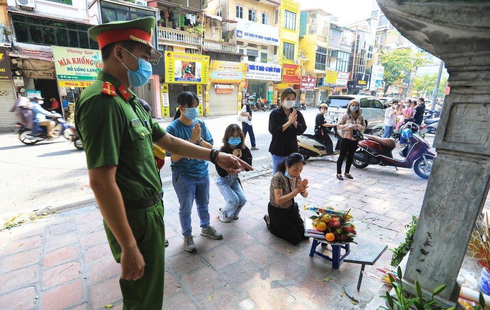 Lực lượng Công an phường Quốc Tử Giám nhắc nhở người dân không tụ tập, đứng giãn khoảng cách khi làm lễ. (Ảnh: Thành Đạt/TTXVN)