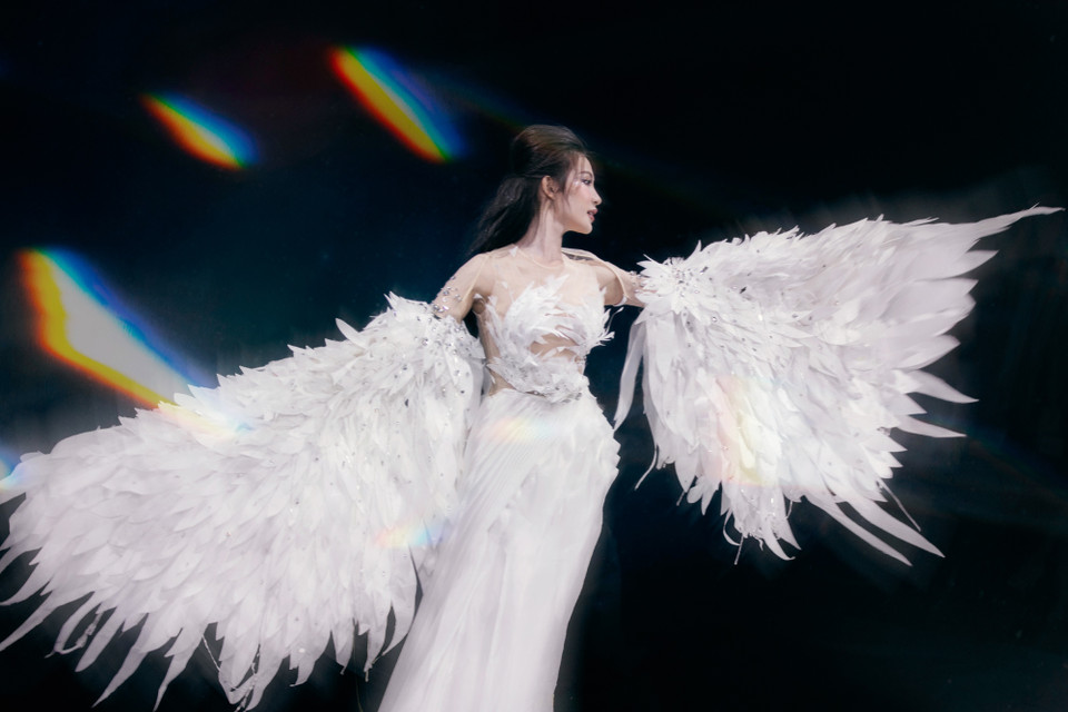 Mở màn cho show diễn, nàng thơ xứ Nghệ - Minh Anh hóa thân thành thiên sứ với đôi cánh trắng, và bộ váy dài, xẻ tà. Những dải lụa cuốn theo từng nhịp bước uyển chuyển hòa cùng chuyển động của làn váy tơ lụa bóng bẩy được dập ly rẻ quạt, kết hợp cùng sải cánh kiêu sa. Người mẫu như một thiên thần. (Ảnh: CTV/Vietnam+)