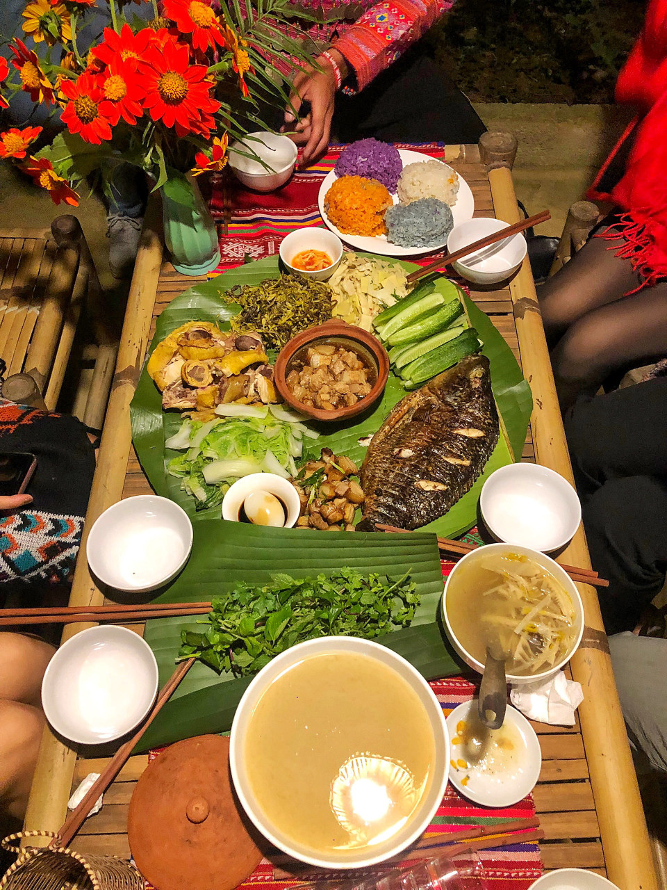  Sau khi lênh đênh trên mặt hồ, đặt chân lên bản cũng là lúc nhá nhem chiều muộn, bà con mang dàn chiêng ra đón khách, và thết đãi chúng tôi bữa tối cỗ lá dân tộc Mường với cá thả hồ nướng mọi, gà đồi, nộm măng chua, nộm tập tàng, xôi ngũ sắc, lợn bản nướng... (Ảnh: Mai Mai/Vietnam+)