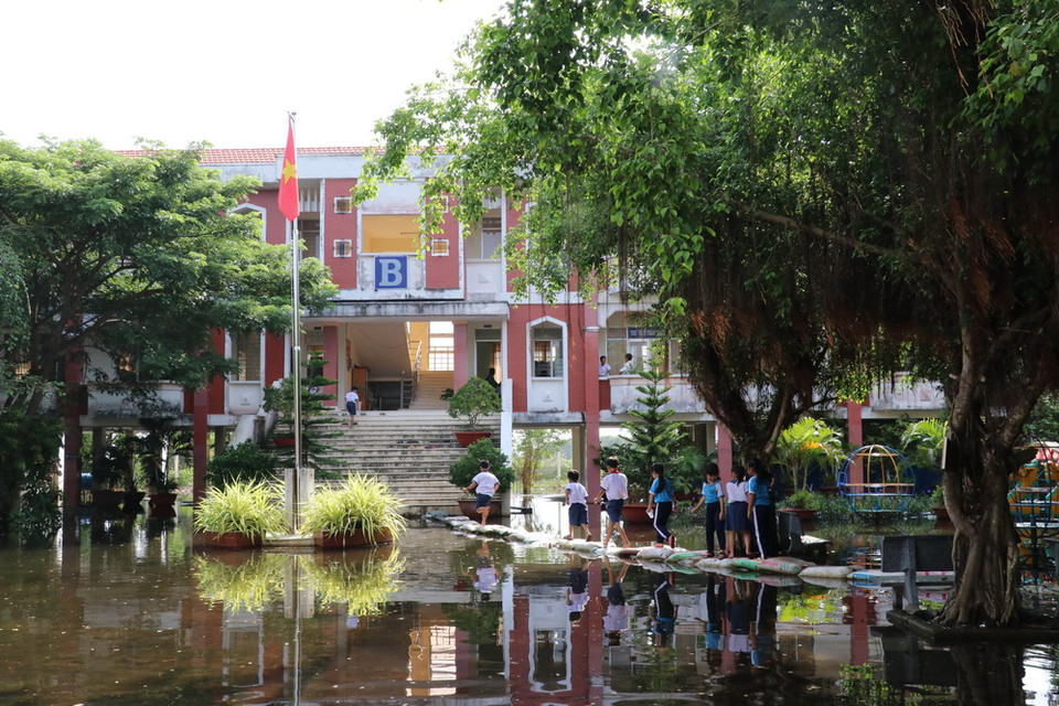 Sân trường Tiểu học Vĩnh Đại (Tân Hưng) ngập trong nước lũ, phụ huynh và giáo viên phải dùng bao cát đắp đường cho các em học sinh đi lại. (Ảnh: Bùi Giang/TTXVN)