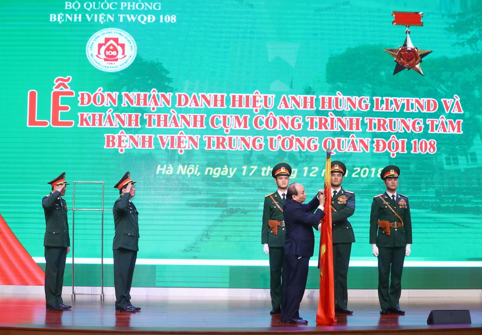 Thủ tướng Nguyễn Xuân Phúc gắn Danh hiệu Anh hùng lực lượng vũ trang Nhân dân thời kỳ kháng chiến chống Pháp lên lá cờ truyền thống của Bệnh viện Trung ương Quân đội 108. (Ảnh: Thống Nhất/TTXVN)