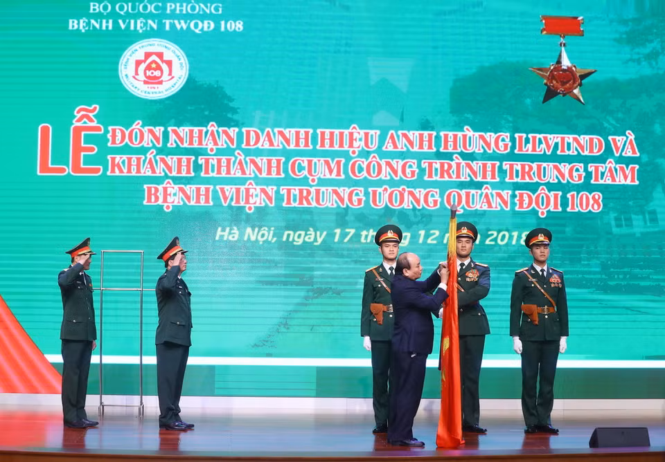 Thủ tướng Nguyễn Xuân Phúc gắn Danh hiệu Anh hùng lực lượng vũ trang Nhân dân thời kỳ kháng chiến chống Pháp lên lá cờ truyền thống của Bệnh viện Trung ương Quân đội 108. (Ảnh: Thống Nhất/TTXVN)