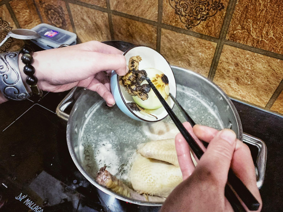 Thả gừng, hành tây, hành khô, hoa hồi vừa nướng vào nồi nước luộc gà. (Ảnh: Mai Mai/Vietnnam+)