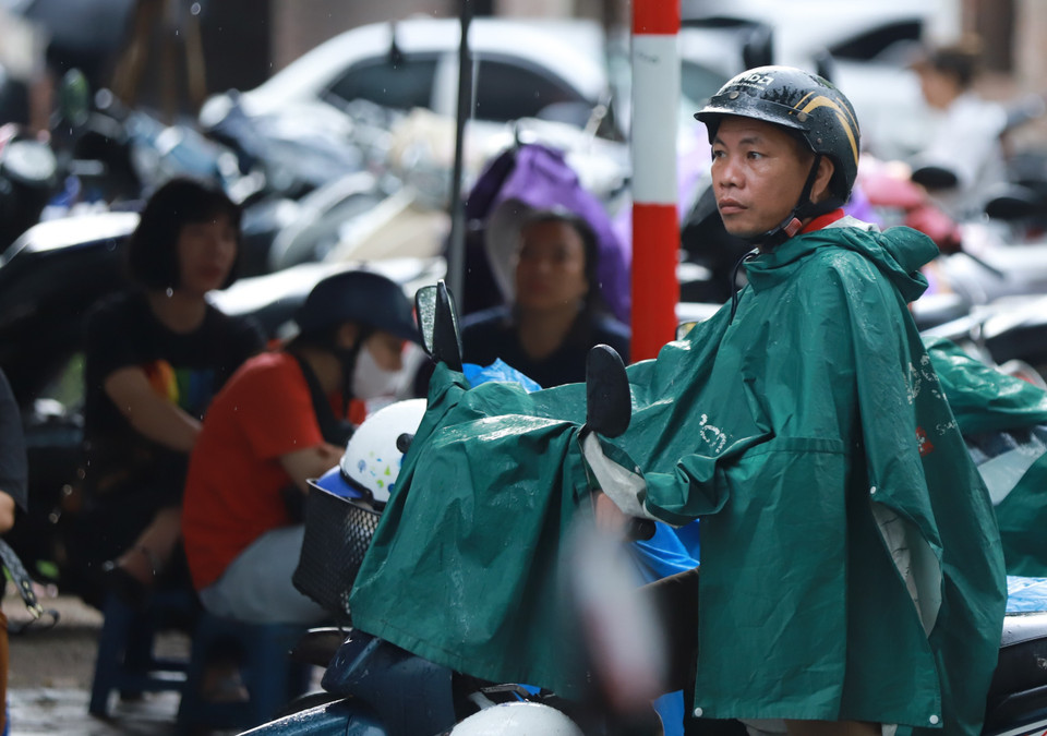 Phụ huynh đội mưa chờ đón con ở bên ngoài điểm thi. (Ảnh: PV/Vietnam+)