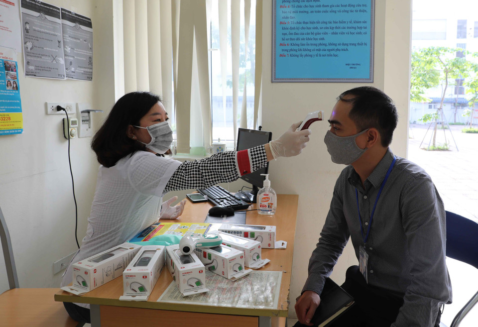 Nhân viên y tế Trường THCS Phan Chu Trinh, quận Ba Đình kiểm tra hoạt động của thiết bị đo thân nhiệt để đưa vào sử dụng khi học sinh đi học trở lại. (Ảnh: TTXVN)