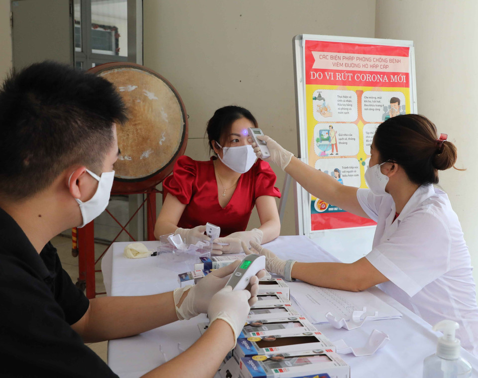 Nhân viên y tế Trường THCS Mạc Đĩnh Chi, quận Ba Đình kiểm tra, hướng dẫn giáo viên sử dụng thiết bị đo thân nhiệt đúng cách. (Ảnh: TTXVN)