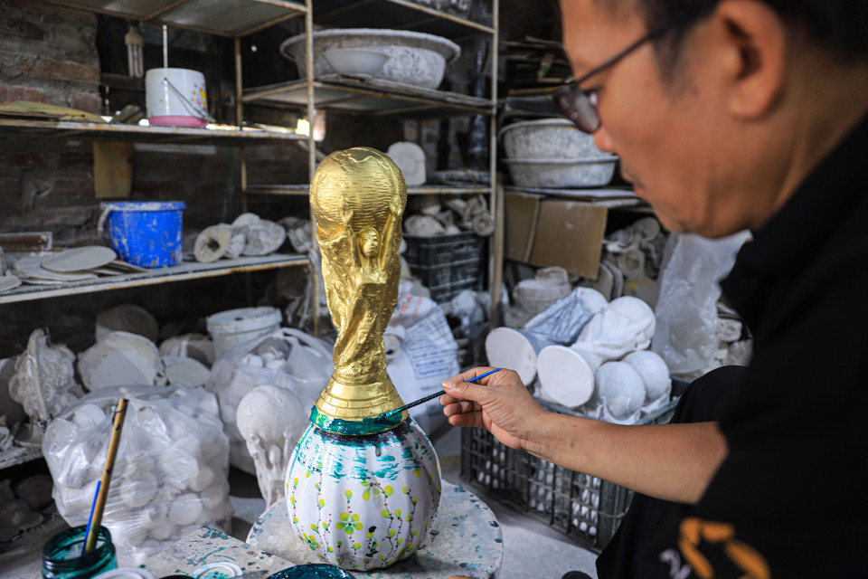 Ông Nhật đang hoàn thiện phần đế của chiếc cúp vàng World Cup 2022 với một lớp sơn màu xanh lá cây. (Ảnh: Việt Anh/Vietnam+)