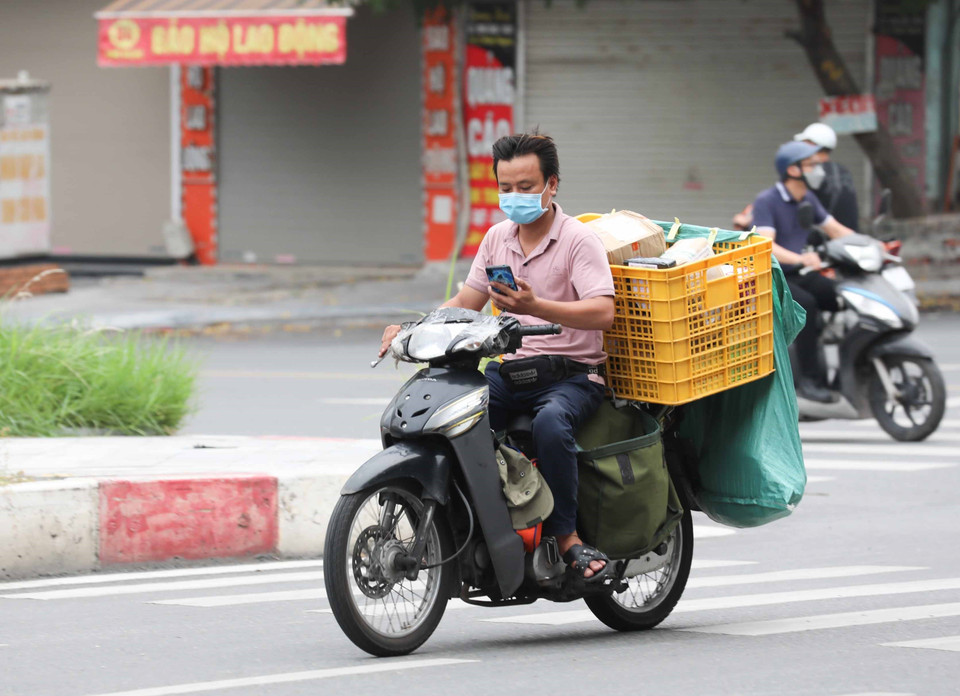Nhân viên giao hàng không đội mũ bảo hiểm lại sử dụng điện thoại khi di chuyển. (Ảnh: Thanh Tùng/TTXVN)