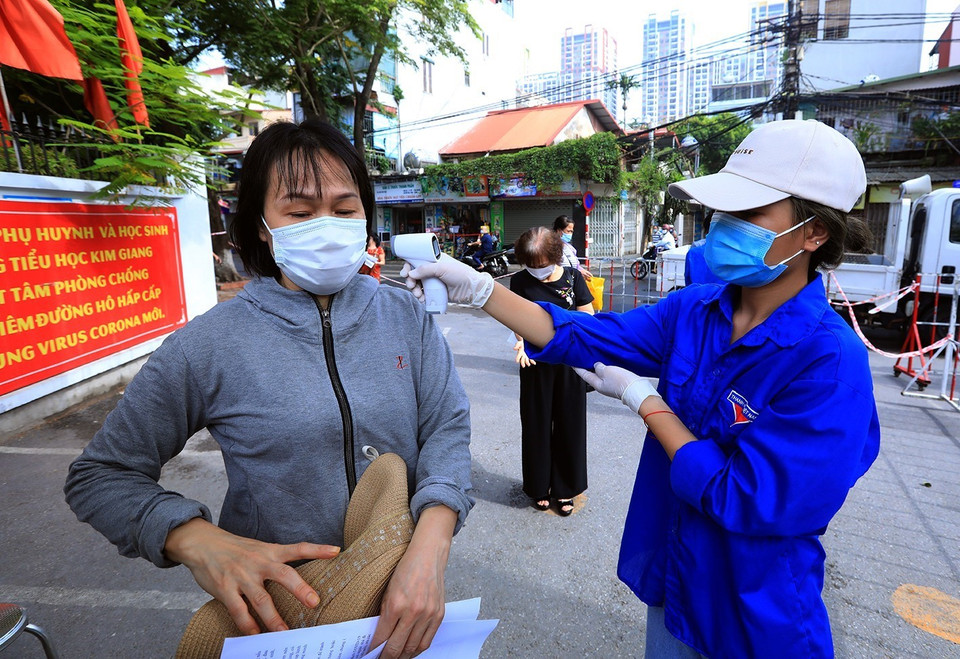 Các tình nguyện viên đo thân nhiệt cho người dân đến tiêm vaccine. (Ảnh: Phan Tuấn Anh/TTXVN)