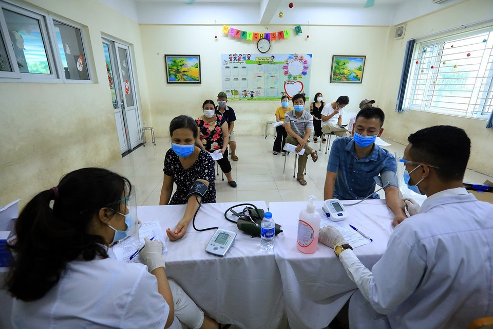 Người dân trước khi tiêm vaccine đều phải đo huyết áp và kiểm tra thân nhiệt. (Ảnh: Phan Tuấn Anh/TTXVN)