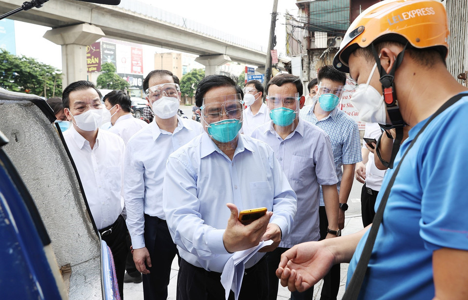 Thủ tướng Phạm Minh Chính kiểm tra giấy phép đi đường và khai báo y tế của một nhân viên giao hàng trên địa bàn quận Thanh Xuân. (Ảnh: Dương Giang/TTXVN)
