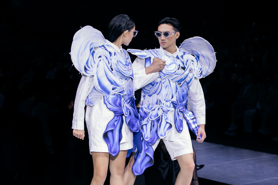 Mở đầu cho bộ sưu tập, bộ đôi Quán quân The Face Vietnam Mạc Trung Kiên và Huỳnh Tú Anh đã xuất hiện ấn tượng trong trang phục thể hiện vẻ uyển chuyển của dòng nước với sắc độ đậm nhạt khác nhau. Chưa dừng lại ở đó, màn tách rời và tạo dáng độc đáo ngay giữa sân khấu của cả hai đã để lại ấn tượng sâu sắc, đồng thời thu hút ánh nhìn của khán giả bằng những sải bước catwalk đầy mạnh mẽ. (Ảnh: CTV/Vietnam+)