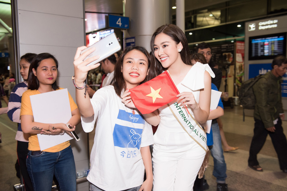 Nàng hậu đeo dải băng Miss International Việt Nam, trên tay cầm lá cờ tổ quốc cùng sự ủng hộ của rất đông người hâm mộ có mặt để tiễn cô lên đường. (Ảnh: CTV/Vietnam+)