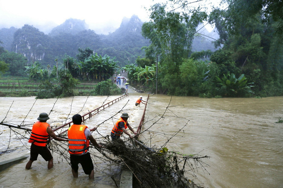 Lực lượng chức năng xã Mai Sao, huyện Chi Lăng vớt rác trôi, mắc vào lan can cầu dân sinh đi vào thôn Nà Lốc - vùng trồng na đặc sản theo quy trình VietGap của huyện Chi Lăng. (Ảnh: Phạm Hậu/TTXVN)