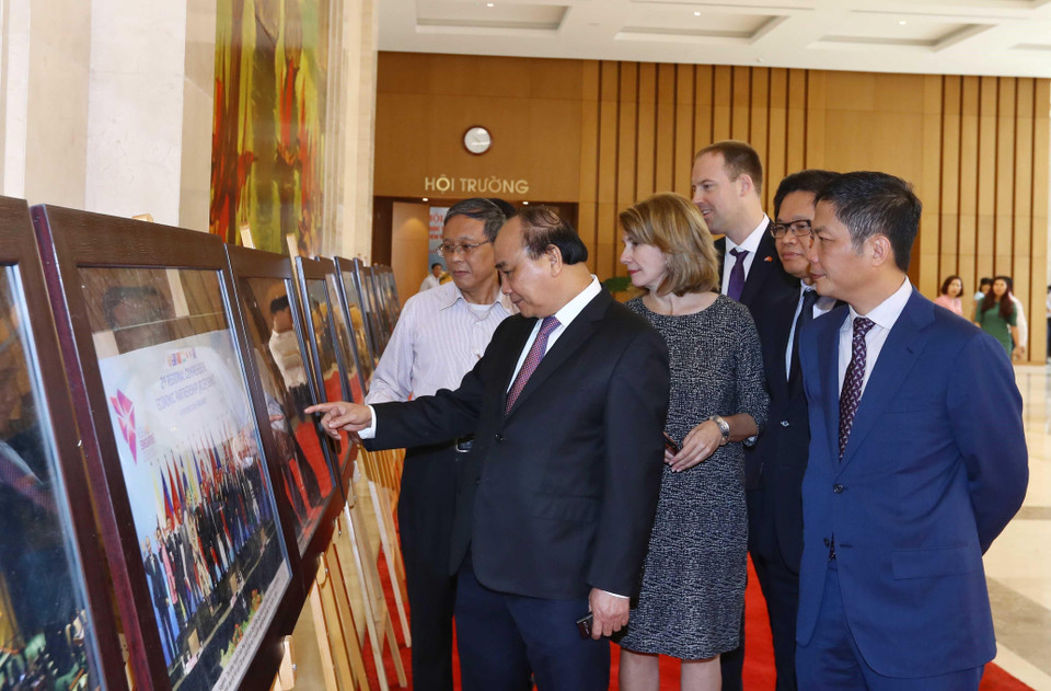Thủ tướng Nguyễn Xuân Phúc, Trưởng Ban Chỉ đạo quốc gia về hội nhập quốc tế và các đại biểu tham quan trưng bày ảnh của TTXVN về hội nhập quốc tế. (Ảnh: Thống Nhất/TTXVN)