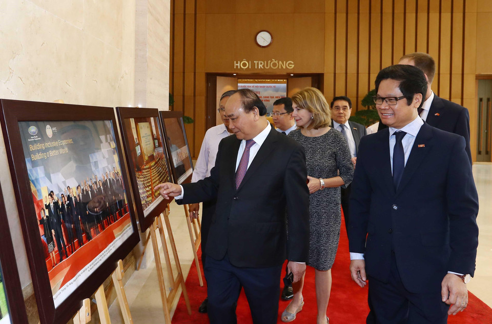 Thủ tướng Nguyễn Xuân Phúc, Trưởng Ban Chỉ đạo quốc gia về hội nhập quốc tế và các đại biểu tham quan trưng bày ảnh của TTXVN về hội nhập quốc tế. (Ảnh: Thống Nhất/TTXVN)