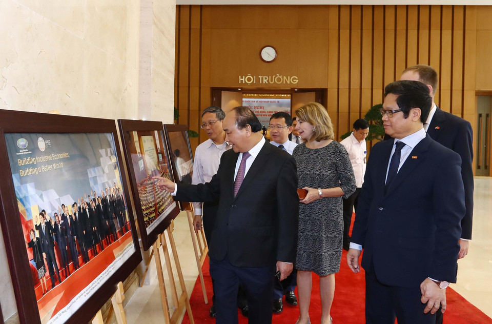 Thủ tướng Nguyễn Xuân Phúc, Trưởng Ban Chỉ đạo quốc gia về hội nhập quốc tế và các đại biểu tham quan trưng bày ảnh của TTXVN về hội nhập quốc tế. (Ảnh: Thống Nhất/TTXVN)