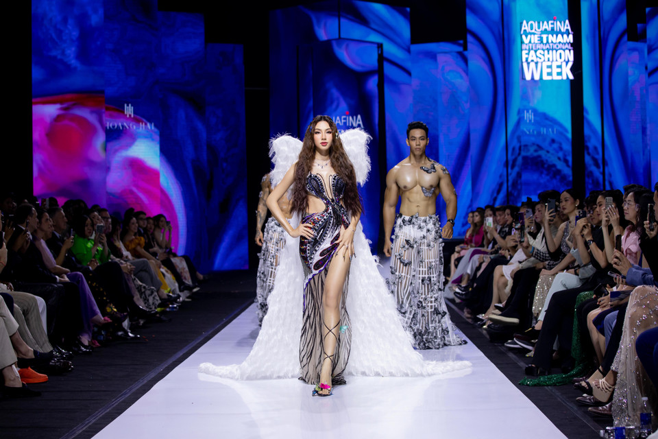 Khép lại show diễn, Miss Grand International 2021 Thùy Tiên khoác lên mình chiếc đầm dạ hội được cắt xẻ táo bạo đính kết các chi tiết đá lấp lánh cùng với đôi cánh lấy cảm hứng từ loài bướm xinh đẹp. Đây là lần đầu tiên Miss Grand International 2021 Thùy Tiên đến với Tuần lễ Thời trang quốc tế Việt Nam trong vai trò vedette của nhà thiết kế Hoàng Hải. Trong thiết kế mang tông màu đen chủ đạo kết hợp với đôi cánh thiên thần, nàng hậu catwalk với thần thái như hóa thân thành ‘nữ hoàng’ được hai ‘vệ sỹ’ hộ tống. (Ảnh: CTV/Vietnam+)