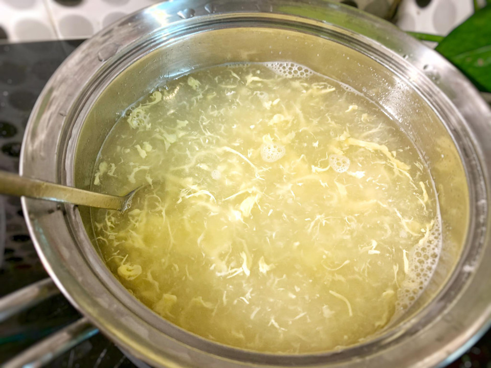 Cho hai bát nước dashi vào nồi, cho hạt quinoa vào, cùng khoảng 20ml nước pha bột năng, quấy đều lên rồi cho lòng đỏ trứng gà vào khuấy đều 1 chiều. Tiếp đến cho tôm, cua, cà rốt vào nấu khoảng 1 phút rồi tắt bếp, thêm hành lá, rau mùi. (Ảnh: Vietnam+)