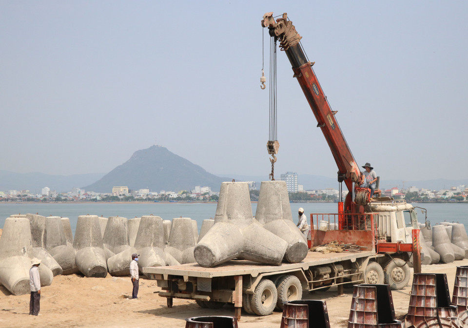 Các trụ bê tông chắn sóng nặng hàng tấn được vận chuyển lên xe tải thi công kè Đà Diễn. (Ảnh: Phạm Cường/TTXVN)