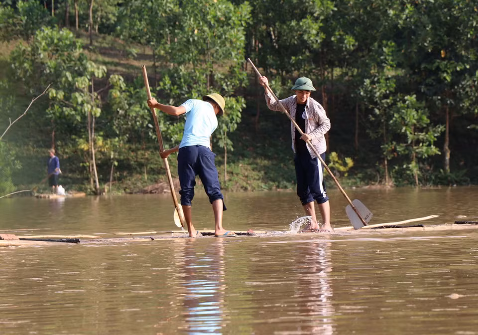 Hai thanh niên đi qua lòng hồ thủy điện bằng phương tiện bè mảng thô sơ, kích thước và tải trọng rất nhỏ. (Ảnh: Xuân Tiến/TTXVN)