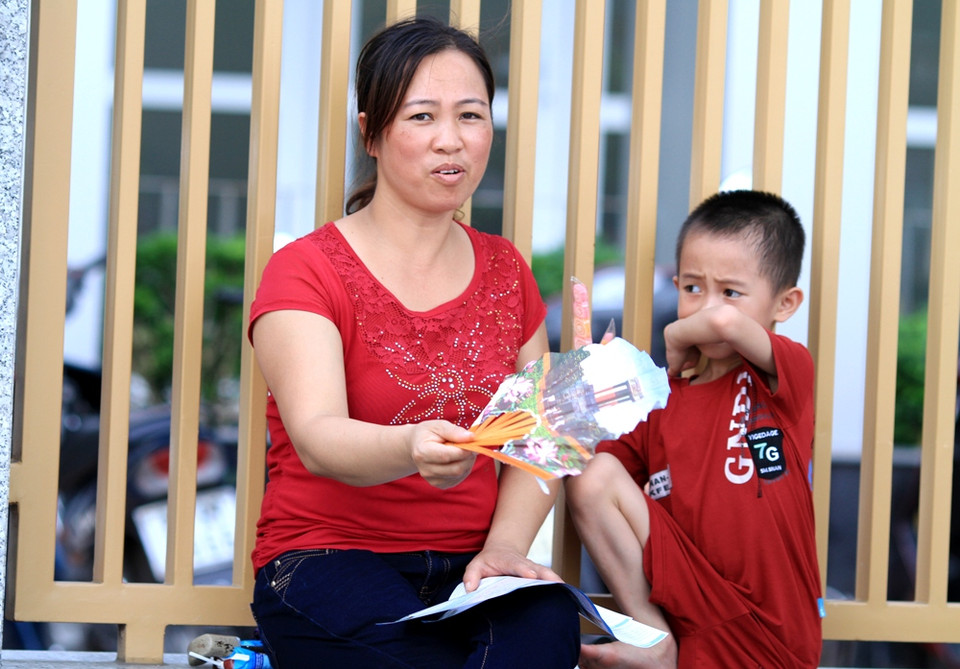 Em bé cũng phải đợi anh cùng mẹ dưới nắng nóng. (Ảnh: Xuân Mai/Vietnam+)