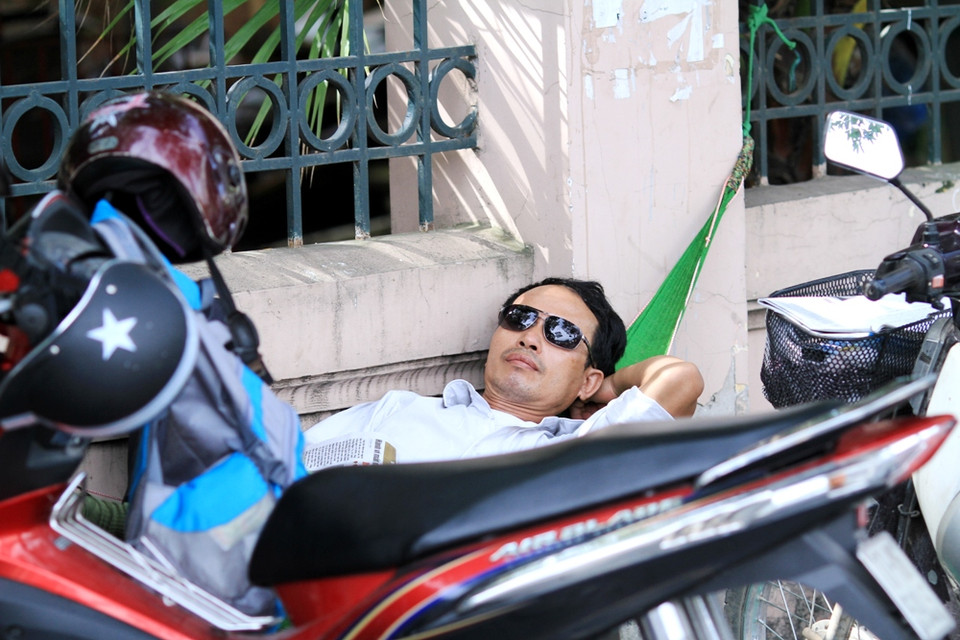 Một phụ huynh mắc luôn võng đợi con trước cổng trường. (Ảnh: Xuân Mai/Vietnam+)